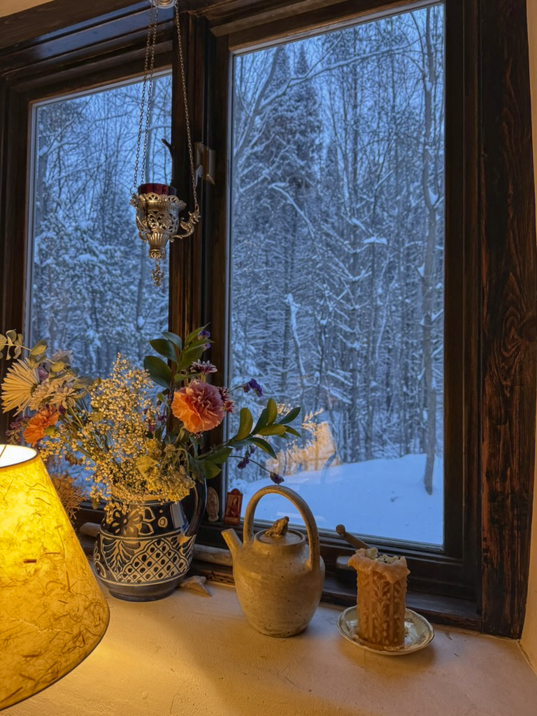 A lamp, flowers and a teapot by the window, snow outside