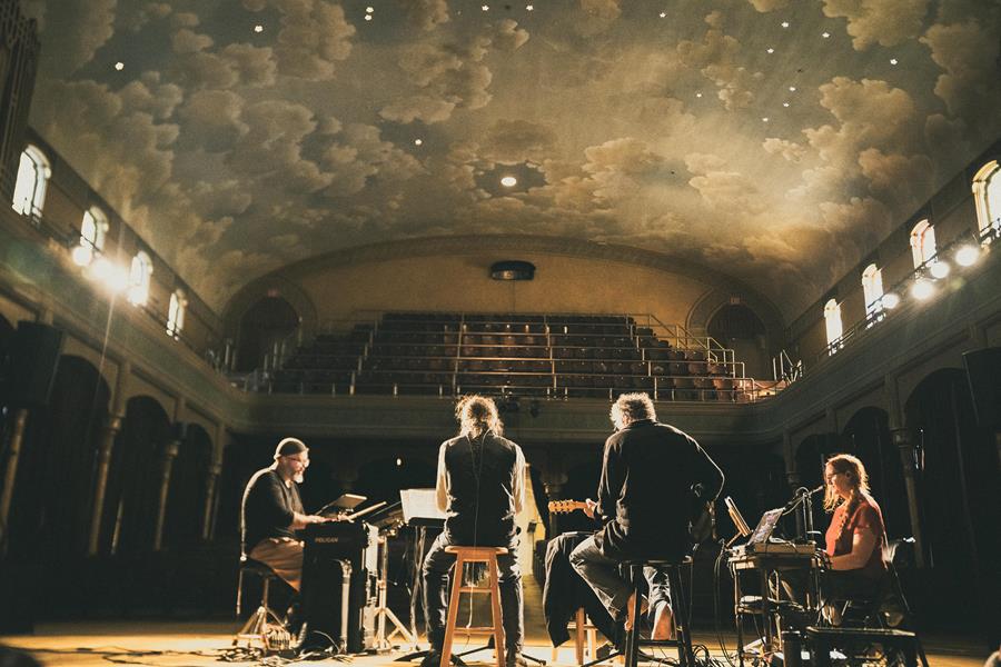 The Nights of Grief and Mystery band on stage beneath a painted cloud ceiling